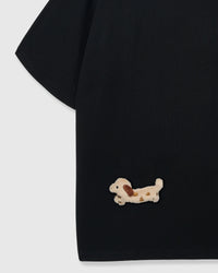 Detail of hand-stitched spotted dachshund on lower body area of black tee showing long body shape