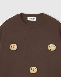 Close-up of plush cookie applique on brown cotton showing smiling face and chocolate chip details