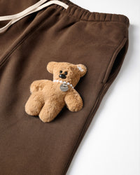 Close-up of plush teddy bear with pearl necklace on brown cotton sweatpant showing 3D texture