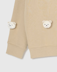 Close-up of plush bear faces near lower hem and sleeve cuff on beige cotton