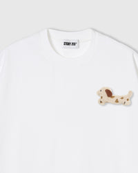 Close-up of spotted dachshund plush on white cotton showing cream body and brown spot markings
