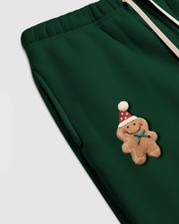 Angled close-up of hand-stitched gingerbread plush on STICKYZOO sweatpant showing icing stitch detail and green bow