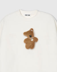 Close-up of plush teddy bear with pearl necklace and ear bow on white cotton sweatshirt showing 3D texture