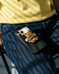 STICKYZOO Honeybuzz Bear Charm Case lifestyle moment, French Alran leather bee bear charm on black case resting on denim