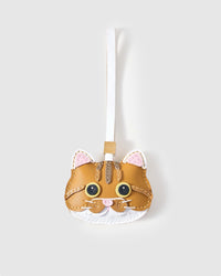 Orange tabby cat charm handmade from French Alran genuine goatskin — caramel-orange body, tabby stripes, gold eyes, white chin, pink nose, cream leather strap. Three days by hand. Arrives in luxury gift packaging. Designed in Amsterdam.