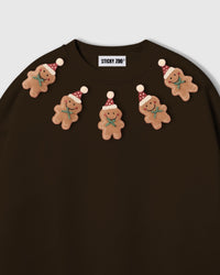 Close-up of plush gingerbread men arc on dark brown sweatshirt showing Santa hats and icing detail
