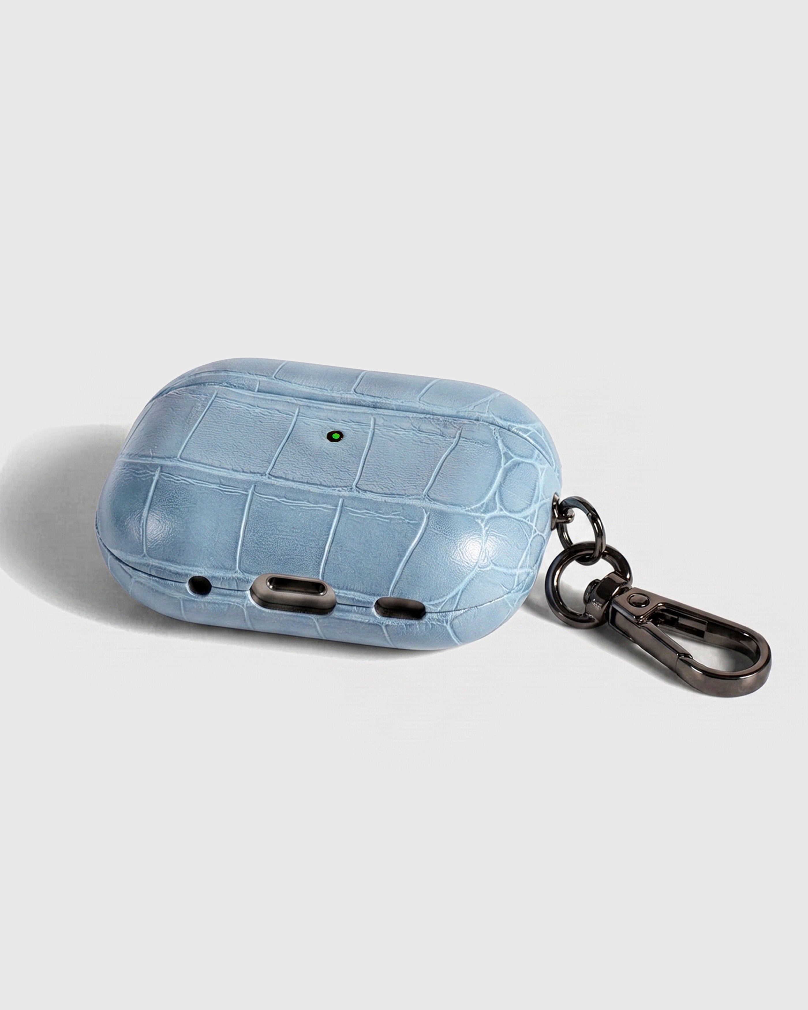 Back view of ice blue croc case showing USB-C port, speaker cutouts, and metal carabiner