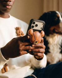 Man holding STICKYZOO Bear Charm Case, French Alran leather bear charm visible, lifestyle moment with dog