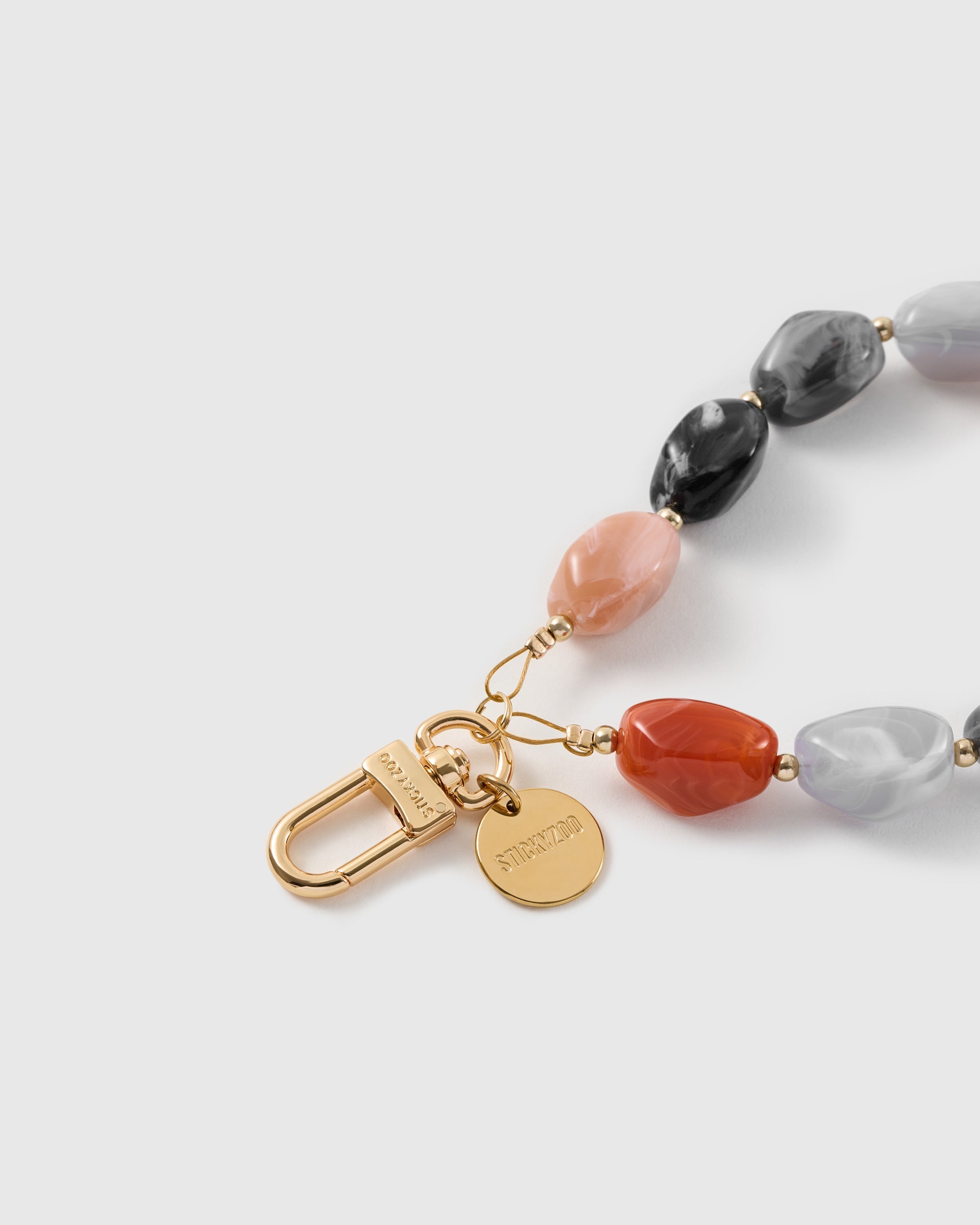 Macro of the 18K gold-plated metal hook and charm disc engraved with STICKYZOO on the beaded agate wrist strap.