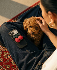 Woman relaxing with STICKYZOO Cherry Charm Case on her lap, French Alran leather cherry charm visible with poodle