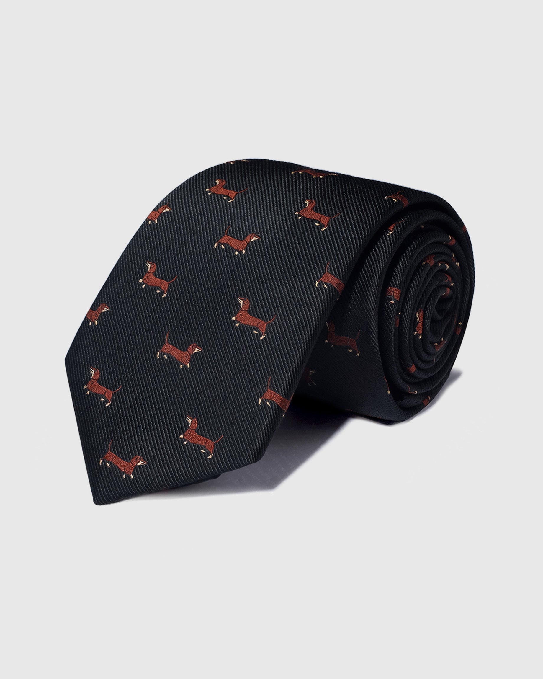 Hand-embroidered silk STICKYZOO Dachshund Tie in black with repeating brown dachshund motifs, rolled to show silk weave and embroidery